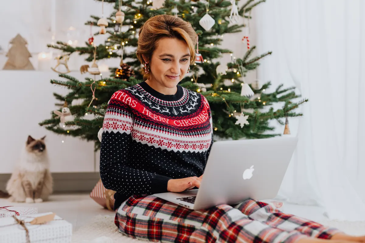 Person plant Weihnachtswünsche am Laptop vor dem Weihnachtsbaum