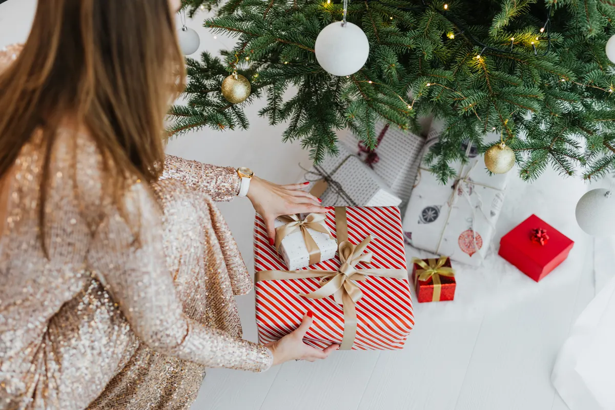 Person legt ein verpacktes Geschenk unter den Weihnachtsbaum Person legt ein verpacktes Geschenk unter den Weihnachtsbaum