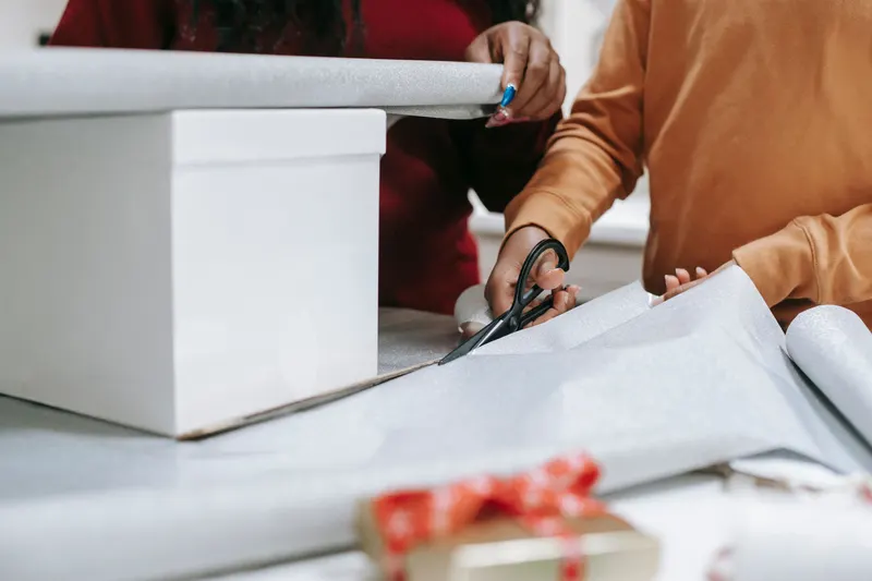 Mehrere Personen packen gemeinsam ein größeres Geschenk Mehrere Personen packen gemeinsam ein größeres Geschenk